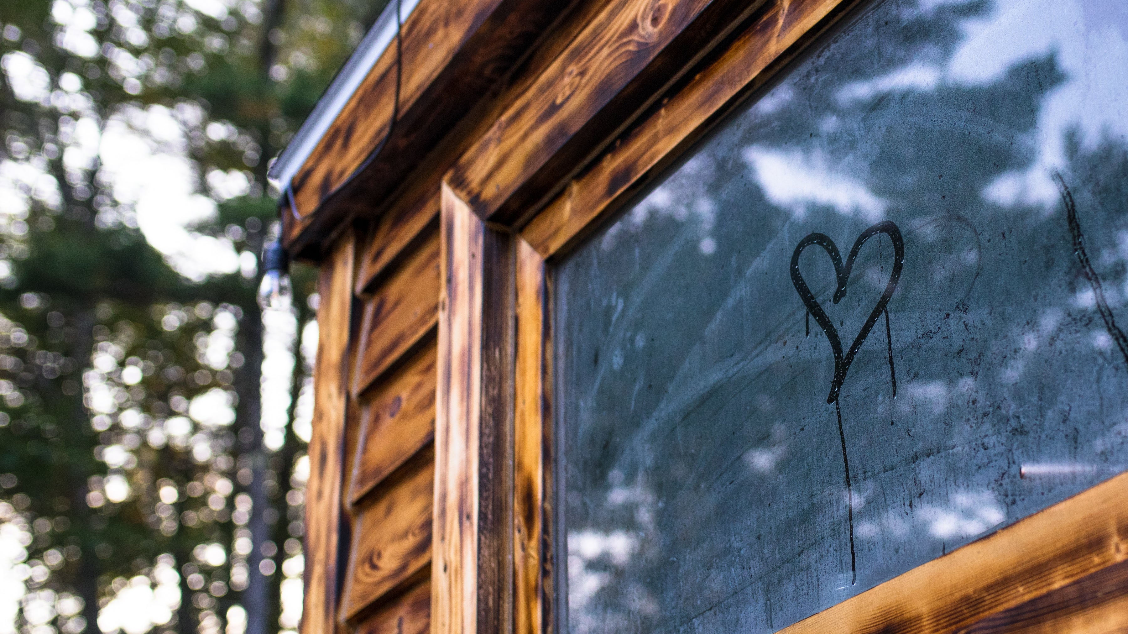 Wooden mobile sauna with a heart drawn on a window in steam, surrounded by trees.