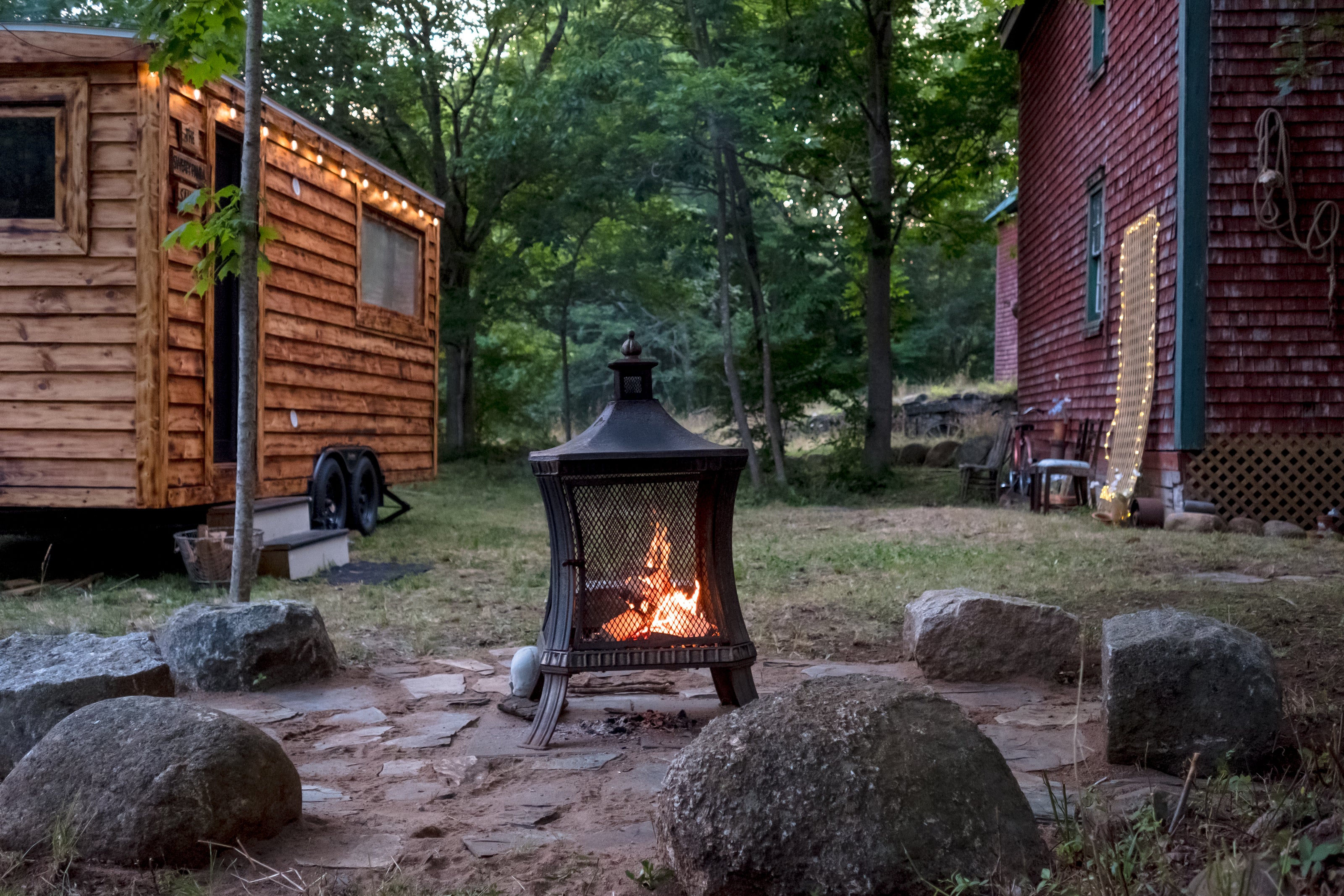 Fire pit in a rustic outdoor setting with mobile sauna and red brick building in the background.